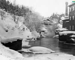 La rivière Magog en hiver, vers 1900. Son fort débit fait en sorte que l’eau ne gèle pas et qu’elle peut alimenter en énergie hydraulique les manufactures situées sur ses rives. Après l’adoption de l’électricité comme principale source d’énergie, ce sont les centrales hydroélectriques qui sont alimentées toute l’année.