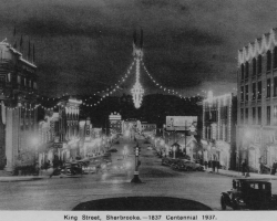 Des photos du centre-ville de Sherbrooke, tout éclairé à l’occasion du « centenaire » de 1937. Les autorités municipales cherchent à stimuler le tourisme et la venue d’industries, entre autres en vantant ses ressources hydroélectriques, et montent de toutes pièces des célébrations du centenaire même si l’année 1937 ne marque le centième anniversaire de rien de significatif...