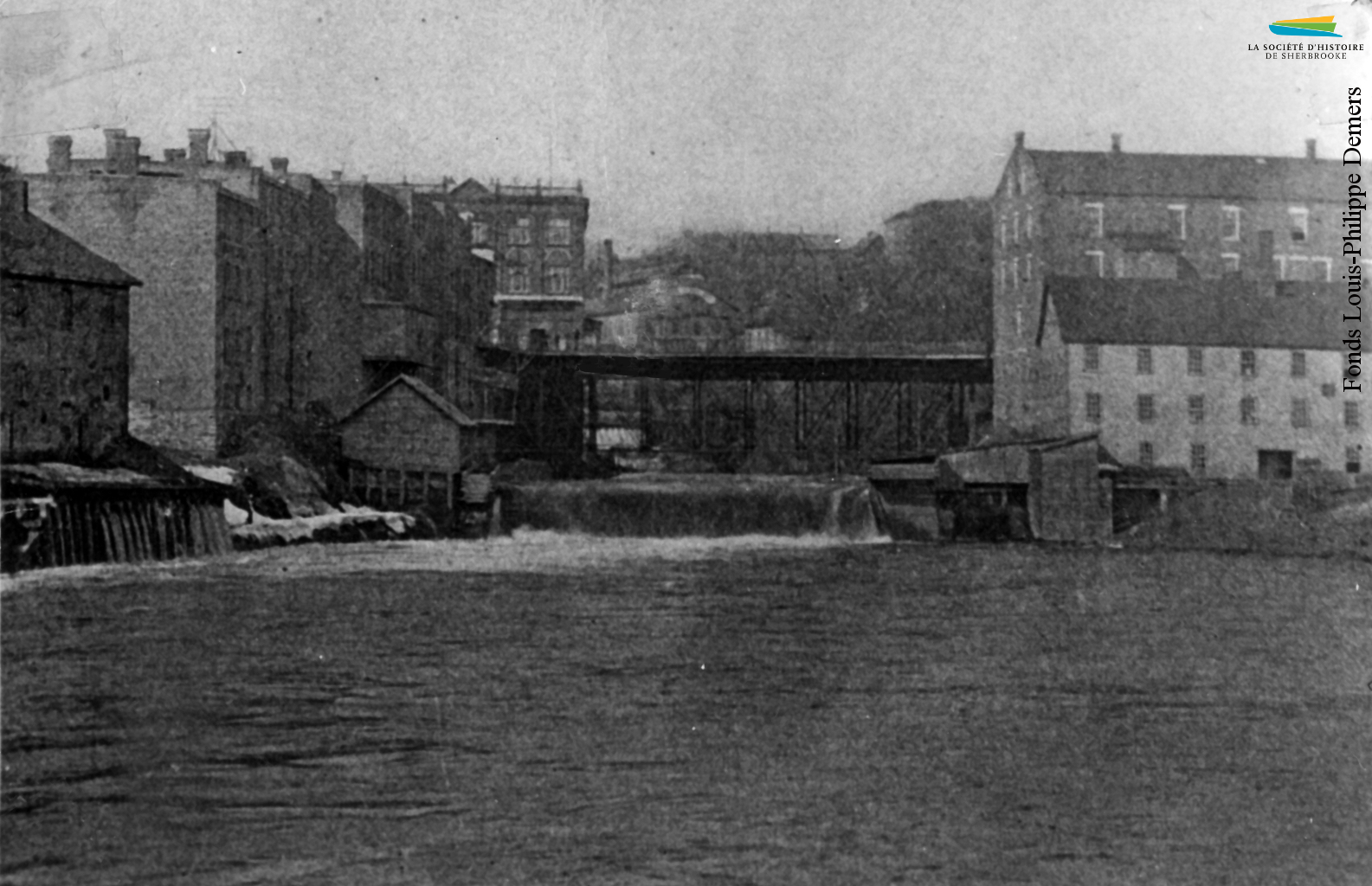 Le site du confluent vers 1898, avec le pont Gilbert-Hyatt et la rue Dufferin. L’usine Sherbrooke Iron Works est située dans le bâtiment blanc à l’avant-plan à droite. Elle y reste jusqu’en 1912.