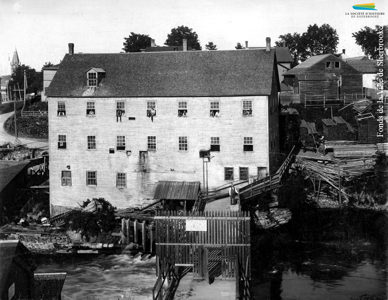L’arrière de la manufacture de portes et fenêtres de <em>G.G. Bryant & Co.</em>, en 1890. Le bâtiment est situé le long de la rue Belvédère Nord, vis-à-vis du barrage no 2, visible au bas de la photographie.
