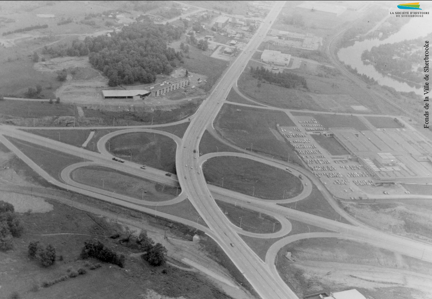 Vue à vol d’oiseau de l’autoroute 410 et de la rue King Ouest, en 1972. Le développement du transport routier crée un nouveau secteur industriel à Sherbrooke, des usines préférant transporter leurs marchandises par camion plutôt que par train. À la droite de la photographie l’on voit l’usine Lowney’s, et sur la gauche l’hôtel le Président.