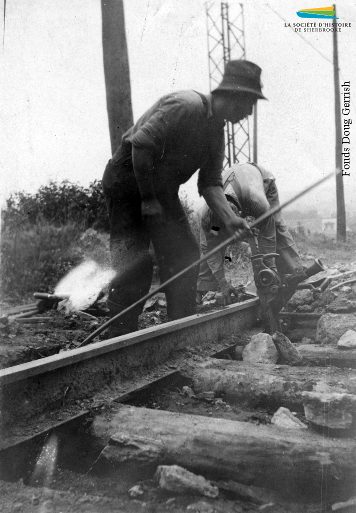 Des ouvriers s’affairent à poser des rails de tramway dans une rue de Sherbrooke, vers 1921. Il s’agit sans doute de la ligne Fairmount, complétée cette même année, qui lie le centre-ville aux rues situées près de la Dominion Textile et de l’Ingersoll-Rand.