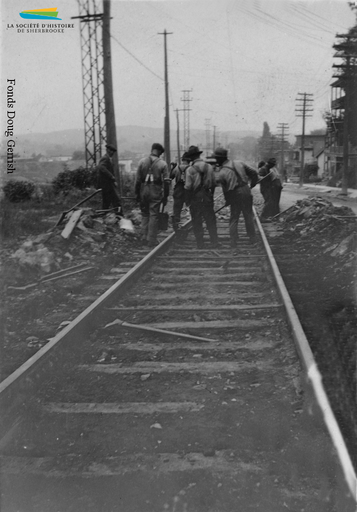 Des ouvriers s’affairent à poser des rails de tramway dans une rue de Sherbrooke, vers 1921. Il s’agit sans doute de la ligne Fairmount, complétée cette même année, qui lie le centre-ville aux rues situées près de la Dominion Textile et de l’Ingersoll-Rand.