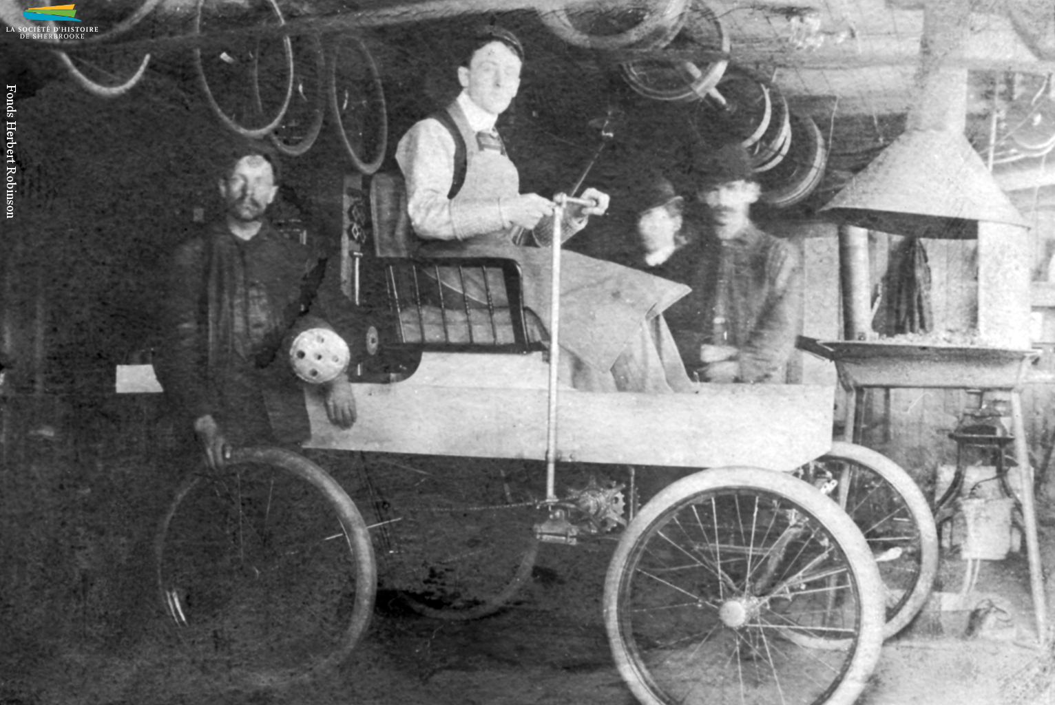 La première voiture à essence construite au Canada serait l’œuvre du Sherbrookois George Foote Foss, qui l’aurait mise au point en 1897. Sur cette photo on voit M. Foss sur sa <em>Fossmobile</em> dans son atelier. Un autre habitant de Sherbrooke, Joseph Fréchette, construit lui aussi une automobile en 1901, et une seconde en 1902.