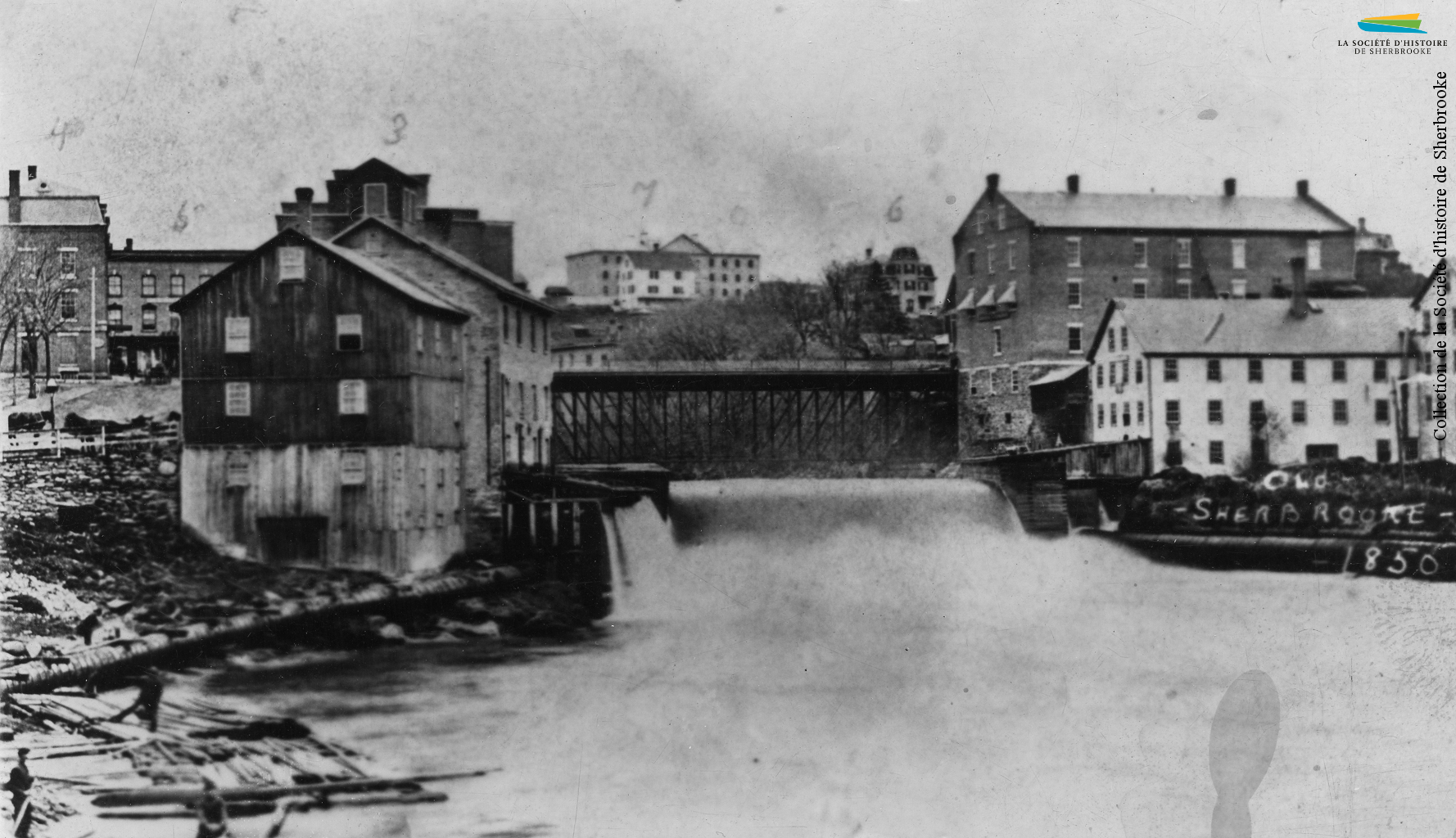 Le barrage no 5 et le confluent des rivières Magog et Saint-François, vers 1885. Le barrage alimente en eau les moulins logés dans les bâtiments situés sur les deux rives. L’eau est alors la principale source d’énergie pour les manufactures de la ville, ce pour quoi celles-ci sont concentrées le long de la rivière Magog.